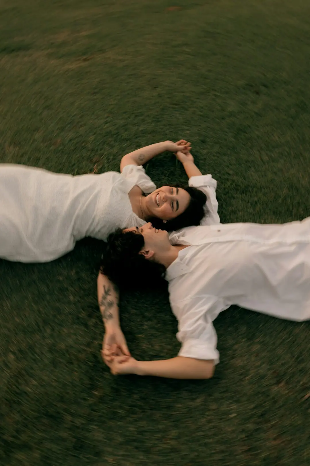 Two happy people in white lying on green grass.